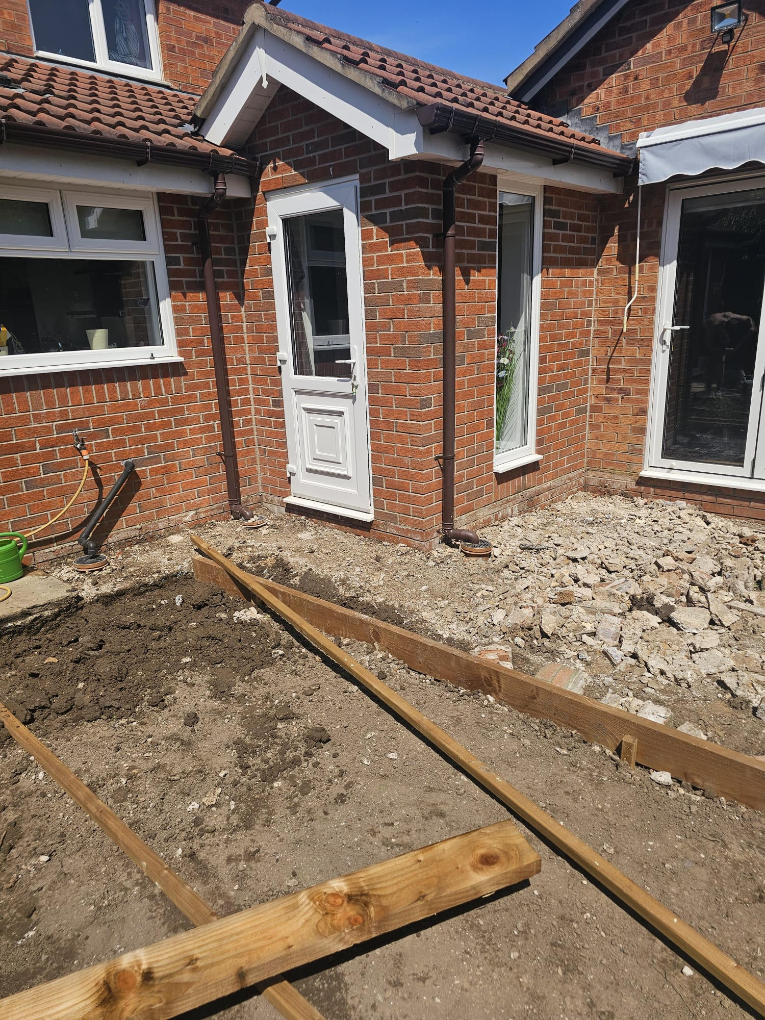 Old patio broken out down to subgrade with timber edging set out around the porch
