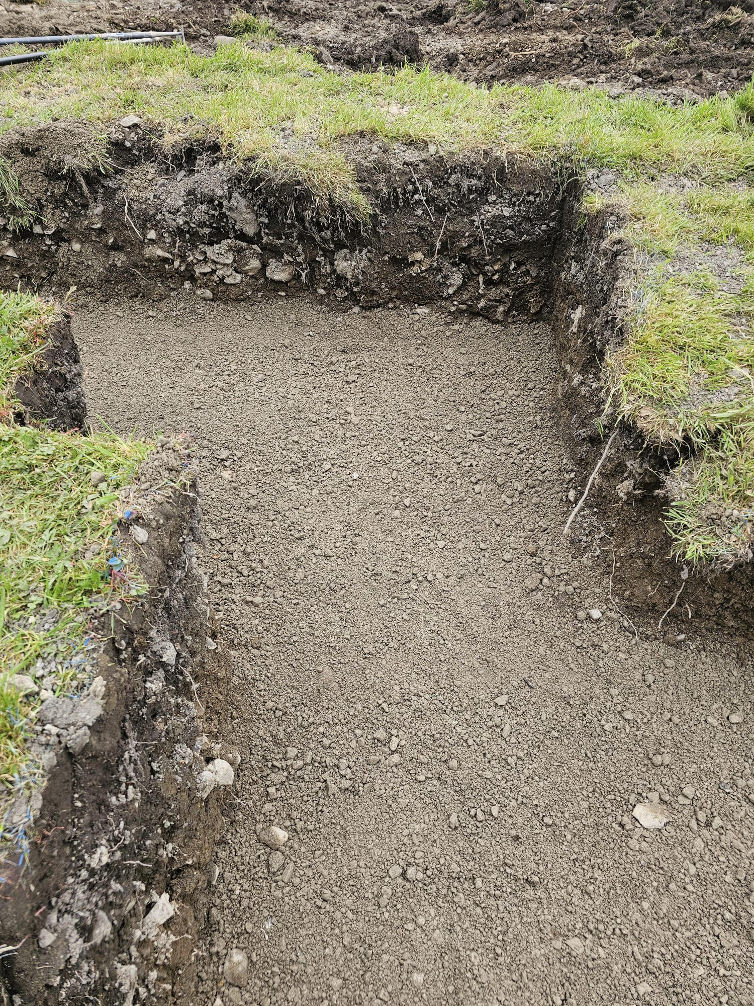 Hand-dug pad foundation with compacted hardcore base