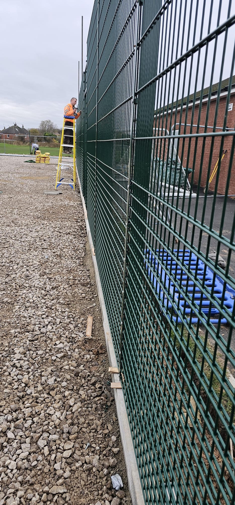 Twin-wire mesh sports fencing being installed on freshly cast concrete plinth