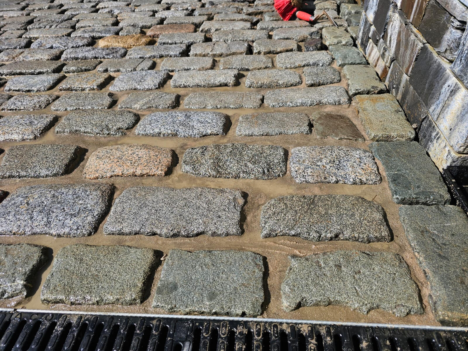 Detail of multi-tone granite cobbles laid against natural stone wall plinth