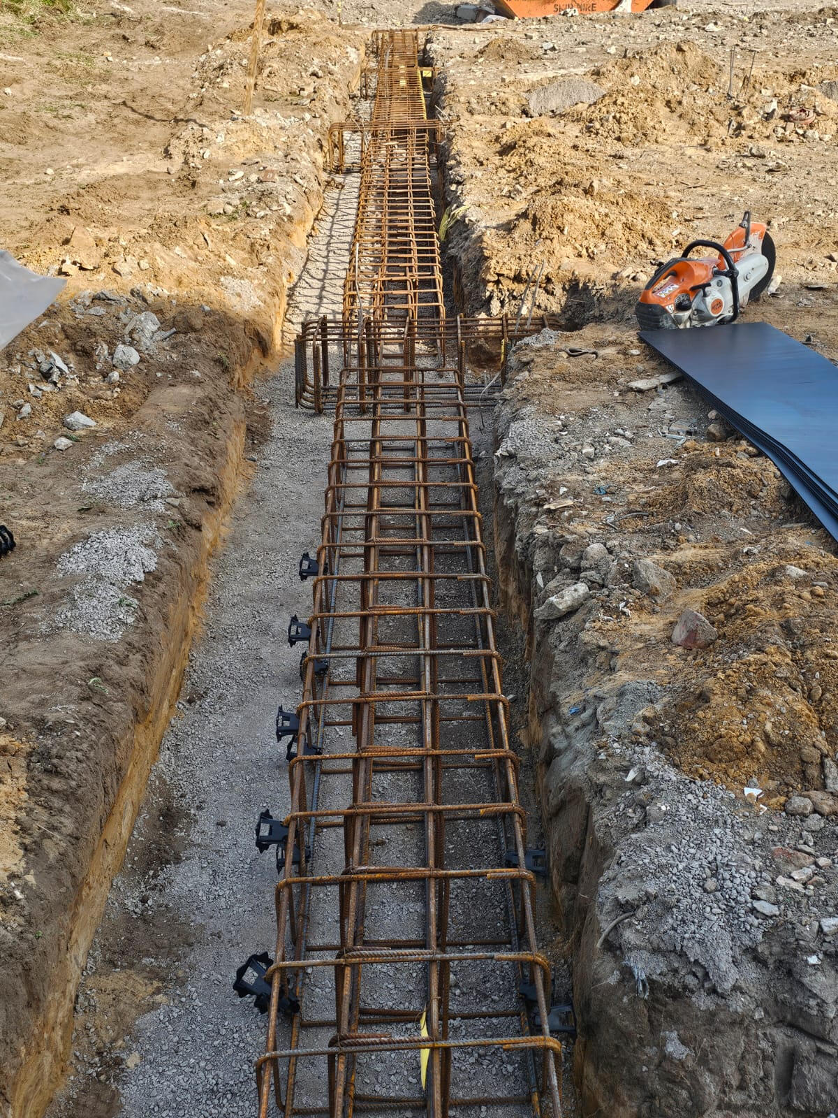 Full rebar cage with spacers sat in a strip footing trench ready for concrete
