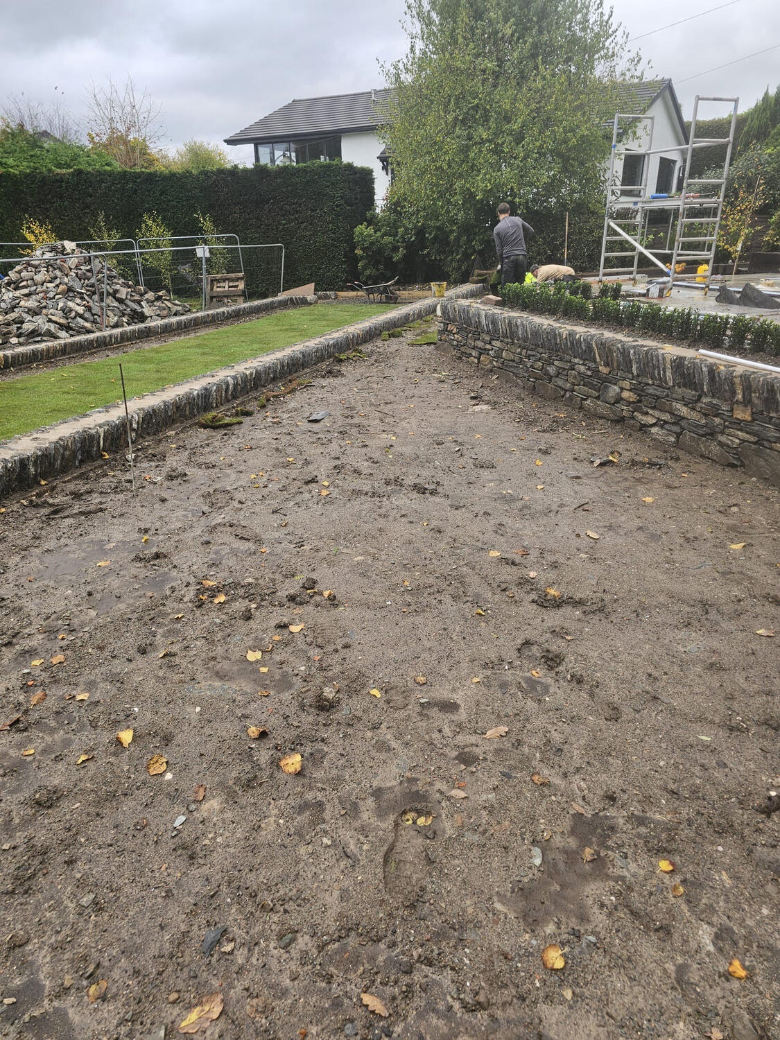 Prepared lawn bed graded between new dry-stone retaining walls ready for turf