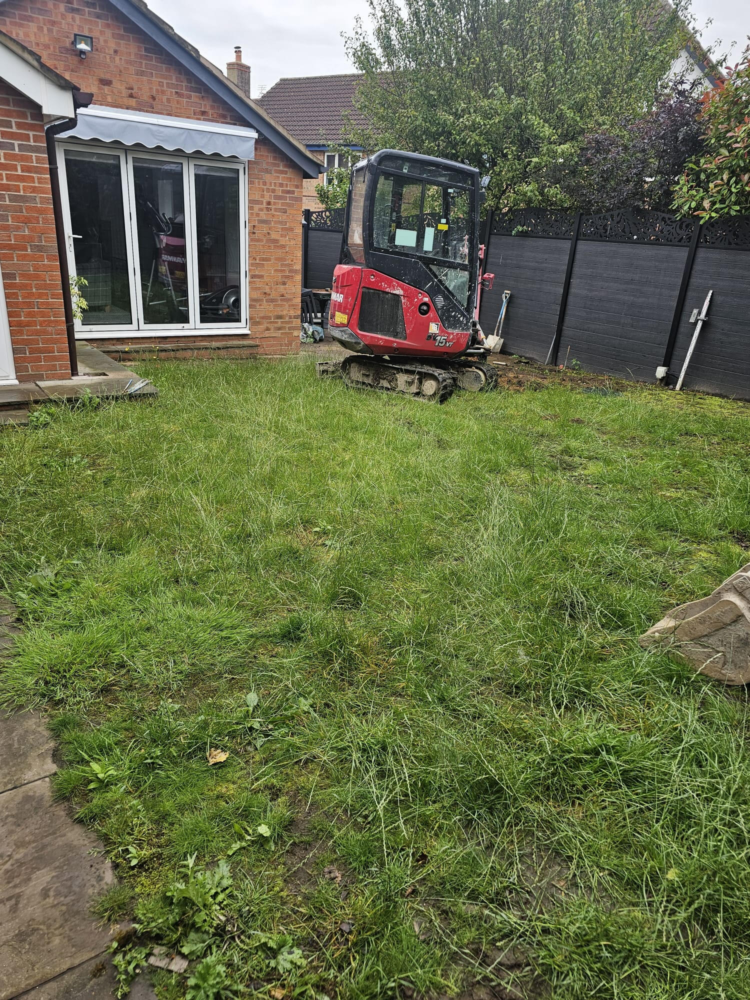 Tired domestic back garden before works with overgrown lawn and mini-excavator on site